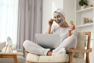 Wall Mural - Young woman with face mask and cucumber slices using laptop at home. Spa treatments