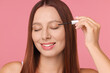 Beautiful woman applying serum onto eyelashes on pink background