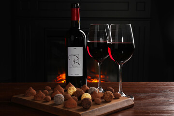 Poster - Red wine and chocolate truffles on wooden table against fireplace