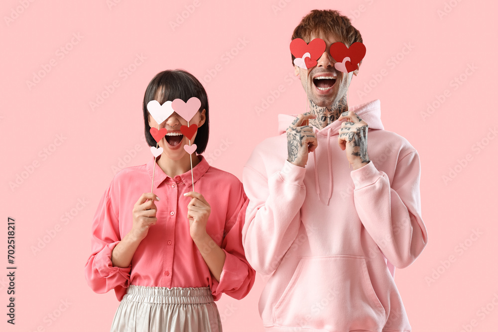 Funny young couple with paper hearts on pink background. Valentine's day celebration