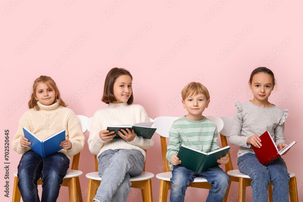 Little children reading books while sitting on chairs against pink background