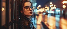 Fashionable brunette girl in trendy clothes and glasses enjoying city nightlife. Beautiful hipster in a leather jacket outside with street lights.