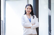 © David - Young happy business asian woman with arms crossed standing int her office and looking at camera.