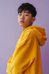 Wall Mural - Asian serious teenage boy wearing yellow hoodie on purple background