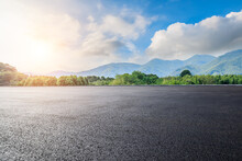 Asphalt Road Square And Green Forest With Mountain Natural Landscape Under Blue Sky