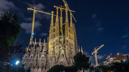 Wall Mural - Sagrada Familia: Day to Night Transition Timelapse of Majestic Roman Catholic Church in Barcelona, Spain. Spires and Cranes Silhouetted Against the Changing Skyline, with Reflections on Serene Lake