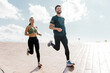 © muse studio - Exuberant couple running together on a bright day, enjoying a healthy lifestyle with a clear blue sky above.