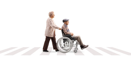 Sticker - Full length profile shot of an elderly woman pushing an elderly man in a wheelchair at a pedestrian crossing