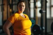 © photolas - Very fat young woman with a sad face stands in the fitness center next to dumbbells and barbells. Unsporty girl at her first workout in the gym.