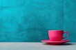 a pink cup and saucer sitting on a table in front of a teal colored wall with a blue background.