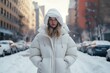 © Ari - Woman standing on a snow-covered street in a white puffy jacket with the hood up.