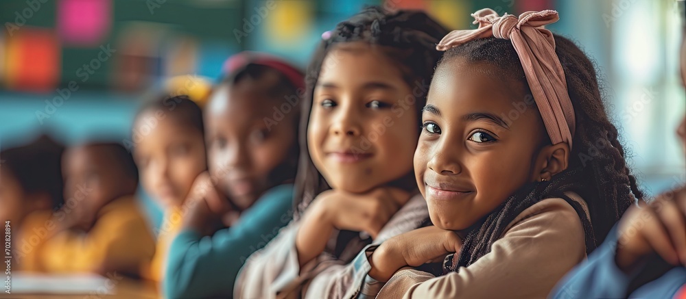 Happy diverse schoolgirls sitting at desks and raising hands in ...