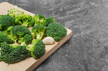 Wall Mural - Broccoli florets and garlic cloves on wooden board. Dark background. Simple ingredients for health.