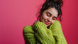 A cheerf young woman enjoys pleasant memories wears a soft comfortable green sweater and round spectacles keeps eyes closed smiles pleasantly isolated over pink background recalls nice moment in life