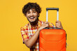 Traveler smiling Indian man wear shirt casual clothes hold suitcase isolated on plain yellow background studio. Tourist travel abroad in free spare time rest getaway. Air flight trip journey concept.