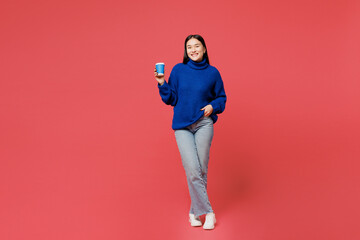 Wall Mural - Full body young happy woman of Asian ethnicity wear blue sweater casual clothes hold takeaway delivery craft paper cup coffee to go isolated on plain pastel pink background studio. Lifestyle concept.