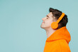 © ViDi Studio - Close up side profile view young man he wearing orange hoody casual clothes listen to music in headphones isolated on plain pastel light blue cyan color background studio portrait. Lifestyle concept.