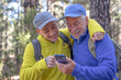 © luciano - Young grandson and old grandfather consulting trail map on mobile phone while hiking together in mountain forest enjoying nature and healthy activity. Adventure has no age