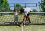 Fototapeta Młodzieżowe - Father teaching his daughter to pick up paddle tennis balls on a tennis court.