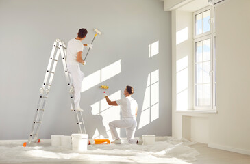 two male workers from the professional home renovation service painting walls light gray in a big br