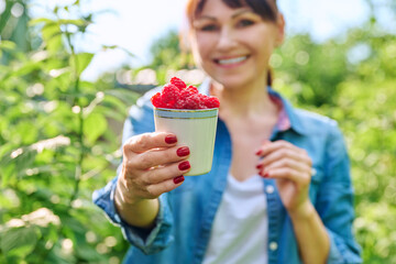 Wall Mural - Close-up of cup with ripe raspberries in hands of woman in summer garden