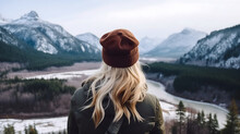 Rearview Photography Of A Carefree Young Woman Looking At The Beautiful Valleys, Snowy Mountains, And Rivers Landscape, Outdoors In Cold Winter, Girl With Blonde Hair Wearing A Jacket And A Cap