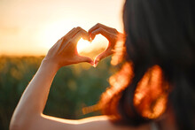 Young Woman Making Heart Shape With Her Hands At Sunset, Love Sign.