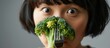 Asian women reluctantly observe broccoli on a fork during mealtime, expressing dislike for vegetables.