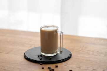 Wall Mural - A cup of coffee laltte with milk on a wooden table with coffee beans against the background of a window.