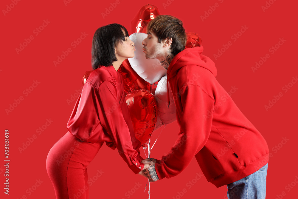 Young couple with heart-shaped air balloons on red background. Valentine's day celebration