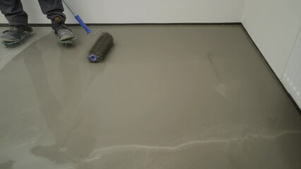 Wall Mural - A worker applies epoxy resin to a new floor. Fill the floor, roll out the mixture with a needle roller. Needle roller when pouring the floor. Needle roller for self-leveling floors. Leveling the floor