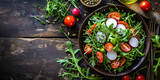 Close up of fresh salad with cherry tomatoes, arugula, radish, avocado and spice, dressing or olive oil on dark wooden background with copy space.
