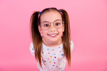 Poster - Photo of adorable small girl with tails hairstyle wear stylish sweatshirt in glasses staring at you isolated on pink color background