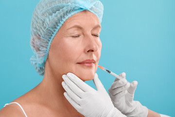 Wall Mural - Doctor giving lips injection to senior woman on light blue background. Cosmetic surgery