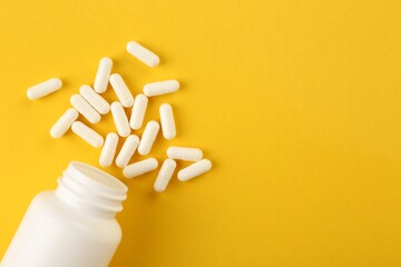 Poster - Bottle and vitamin capsules on yellow background, top view. Space for text