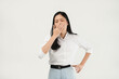 © Illhamt - An Asian woman in a white blouse yawns with one hand covering her mouth and the other on her hip. She looks tired, set against a plain white background, conveying fatigue.