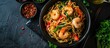 Top view of Mie Goreng, an Indonesian stir-fried dish with prawn noodles and vegetables, served in a black bowl on a dark slate table. Asian cuisine.