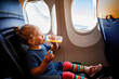 Adorable little girl traveling by an airplane. Small toddler child drinking orange juice sitting near aircraft window. Traveling abroad with kids. Family on summer vacations.