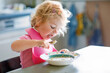 Adorable baby girl eating from spoon vegetable noodle soup. Healthy food, child, feeding and development concept. Cute toddler child with spoon sitting in highchair and learning to eat by itself