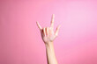 Hand showing rock sign with fingers gesture against pink background, human hand gesture