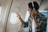 Fototapeta  - Asian man on an airplane looking out the window with headphones on, possibly enjoying music or an audiobook during his flight.