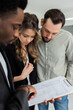 © ABCreative - Smart, elegant African American woman with dark complexion carrying building papers while standing in front of a young couple with a family who are selecting a home for their family.