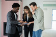 © ABCreative - African American real estate agent with dark complexion demonstrating a new construction plan to clients who are inspecting it while standing in front of their homes and potential future investments.