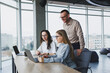 © Дмитрий Ткачук - Three employees in a modern office, a man and a woman work at a table, colleagues discuss and consult, thinking about a joint project.