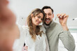 © ABCreative - Having the keys to their new house in their possession, a loving couple embraces hugging. Young just married family obtained a financing, rented a new home, and purchased it. The keys are blurry.
