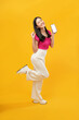 © Illhamt - full-body portrait of an happy Asian woman holding a cell phone on a yellow background