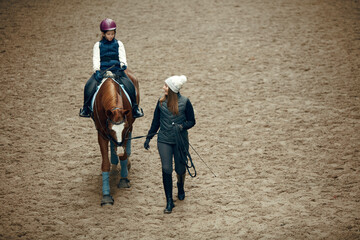 aerial, top view. female teacher, instructor teaching little girl, kid horseback riding. careful rid