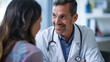 © EmmaStock - A smiling mid adult male doctor listens as a female patient discusses her health