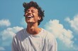 An exuberant young man laughing against a gentle sky blue background.