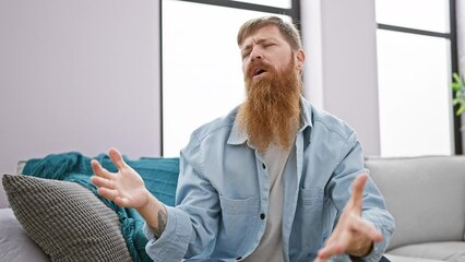 Wall Mural - Cheerful young redhead man confidently speaking, relaxing on a cozy sofa at home, exuding happiness while sitting, a radiant smile gracing his handsome face